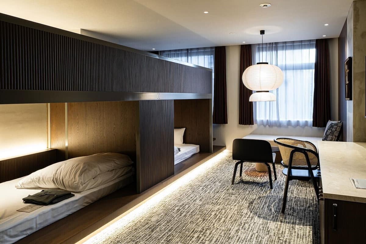 Une chambre dâhĂŽtel moderne avec des lits superposĂ©s, un bureau, des chaises et une grande fenĂȘtre avec des rideaux.