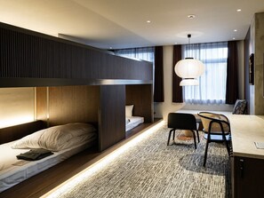 A modern hotel room with bunk beds, a desk, chairs, and a large window with curtains.