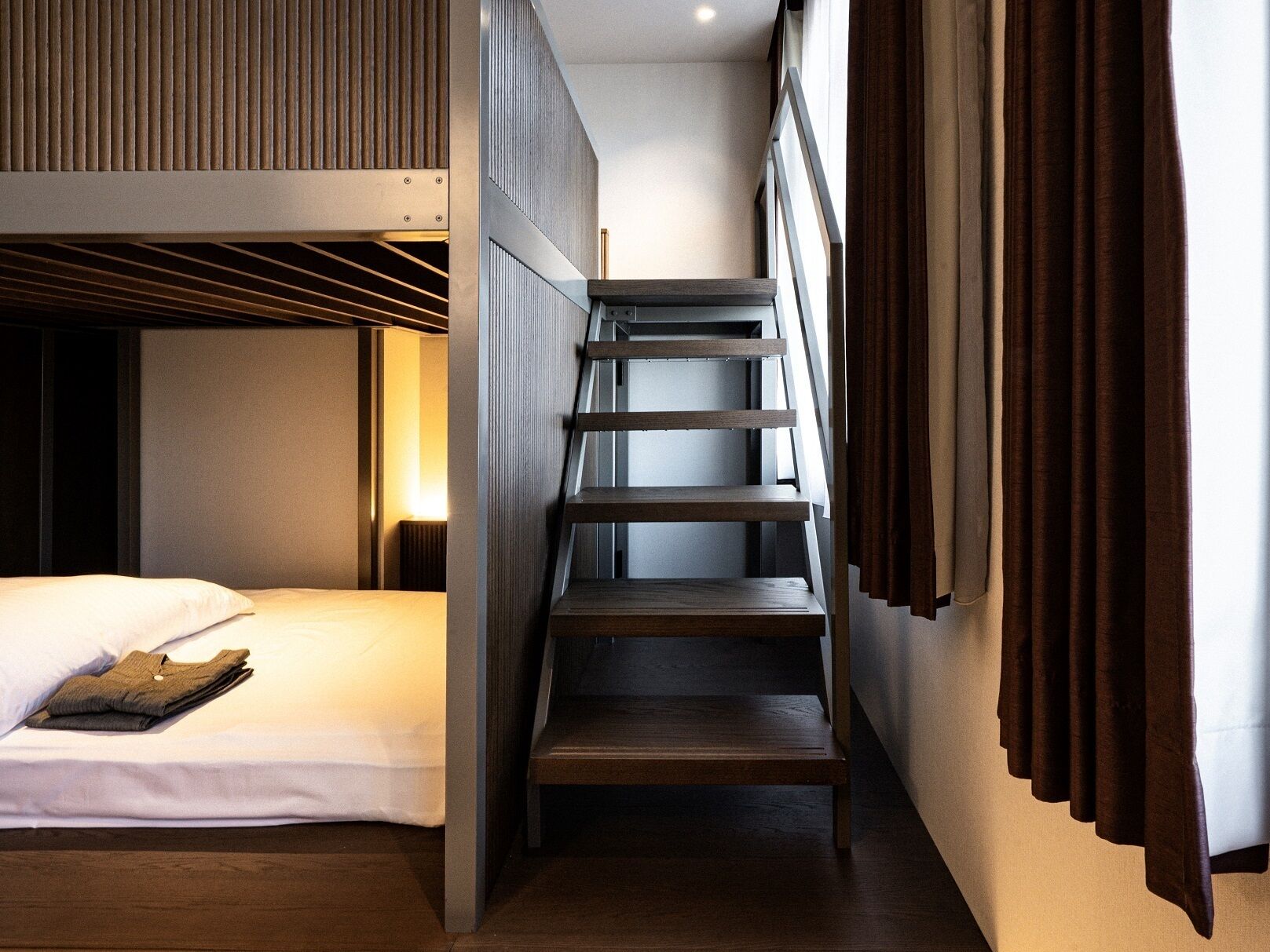 A modern hotel room with a bunk bed, a staircase, and a view of the city.