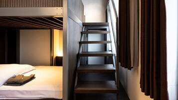 A modern hotel room with a bunk bed, a staircase, and a view of the city.