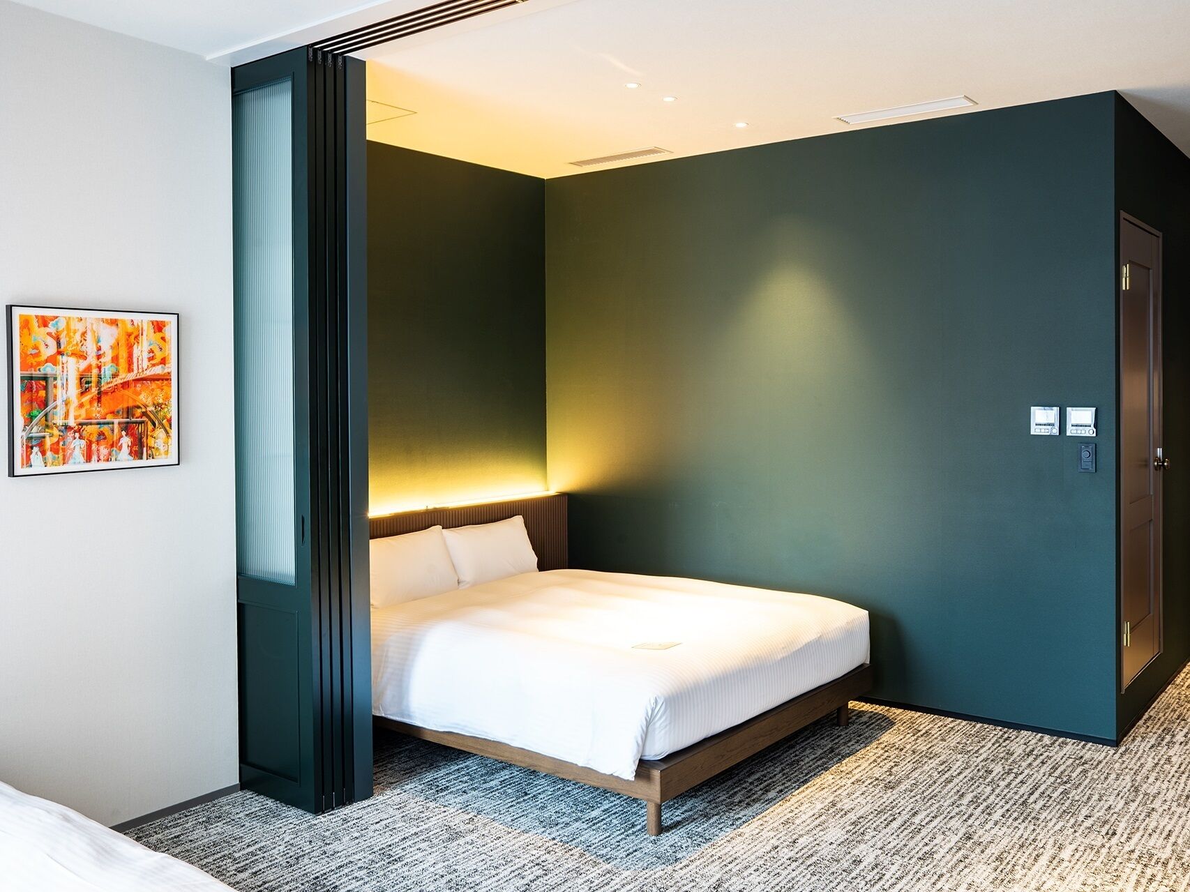 Une chambre d’hôtel avec un lit, un tableau au mur et une porte avec une serrure.