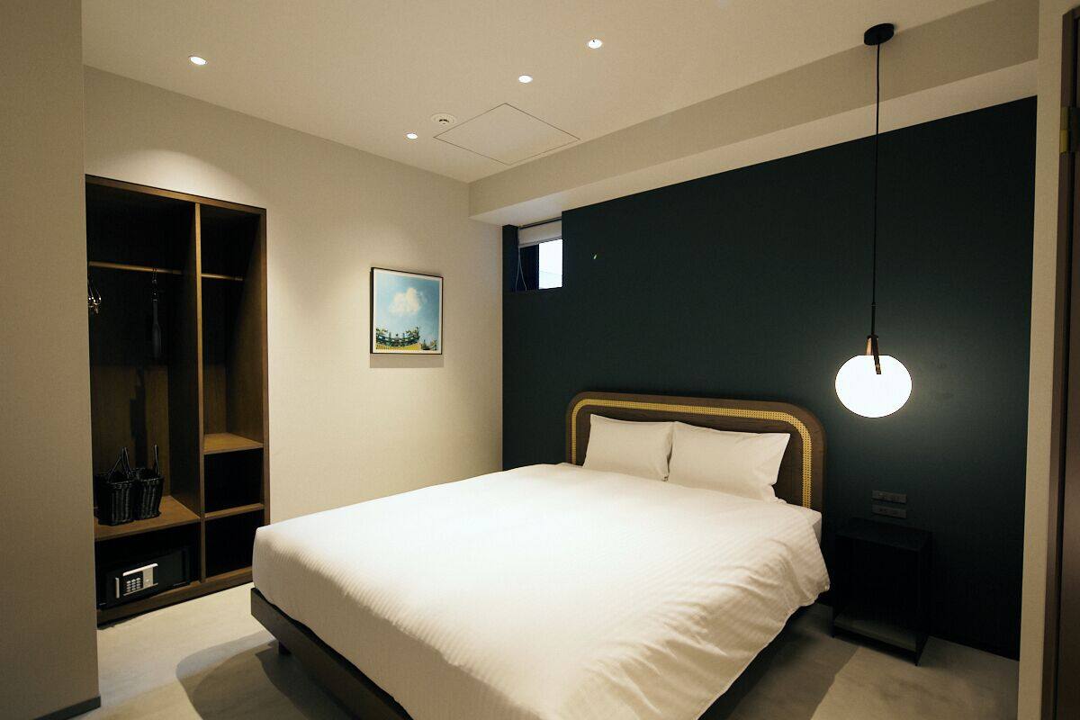 A bedroom with a bed, a wardrobe, a nightstand, and a wall-mounted light fixture.