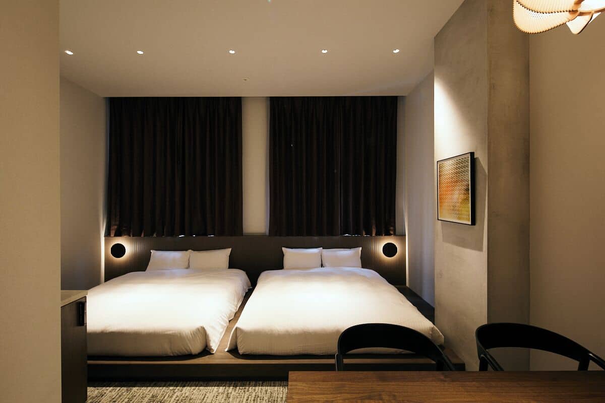 A hotel room with two beds, a wooden table, and a chair.