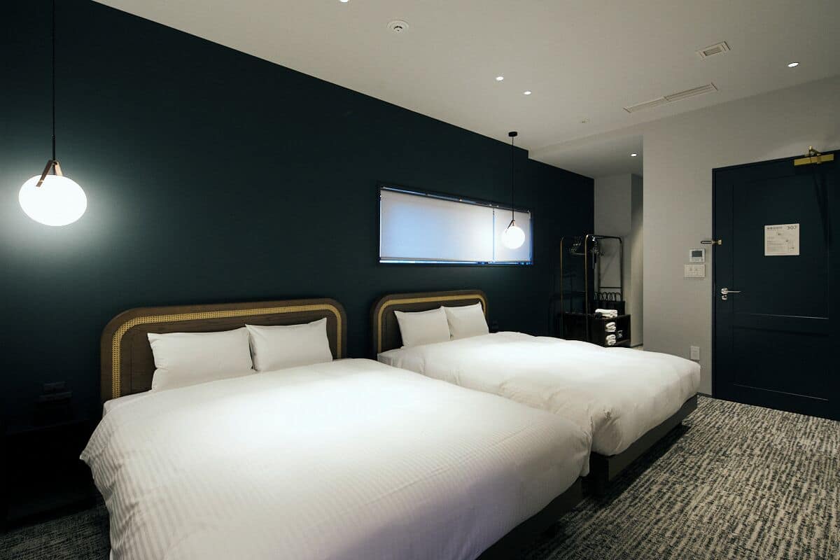 A hotel room with two beds, a dark wall, a window, and a door.