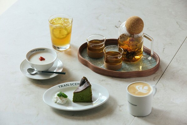 Une table dressée avec une variété de boissons et de desserts, notamment une part de gâteau vert, une tasse de café et un verre de thé.