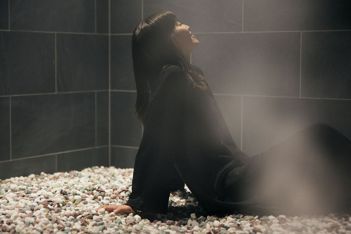 A person sitting on a bed of pebbles in a dimly lit room with tiled walls.