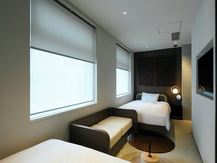 A modern hotel room with two beds, a sofa, a small table, and large windows.