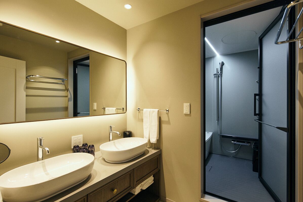A modern bathroom with two sinks, a large mirror, and a shower area.