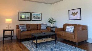 A living room with two brown leather sofas, a coffee table, a lamp, framed pictures, and a potted plant. - Renovated In-Town Bungalow in French Lick (French Lick)