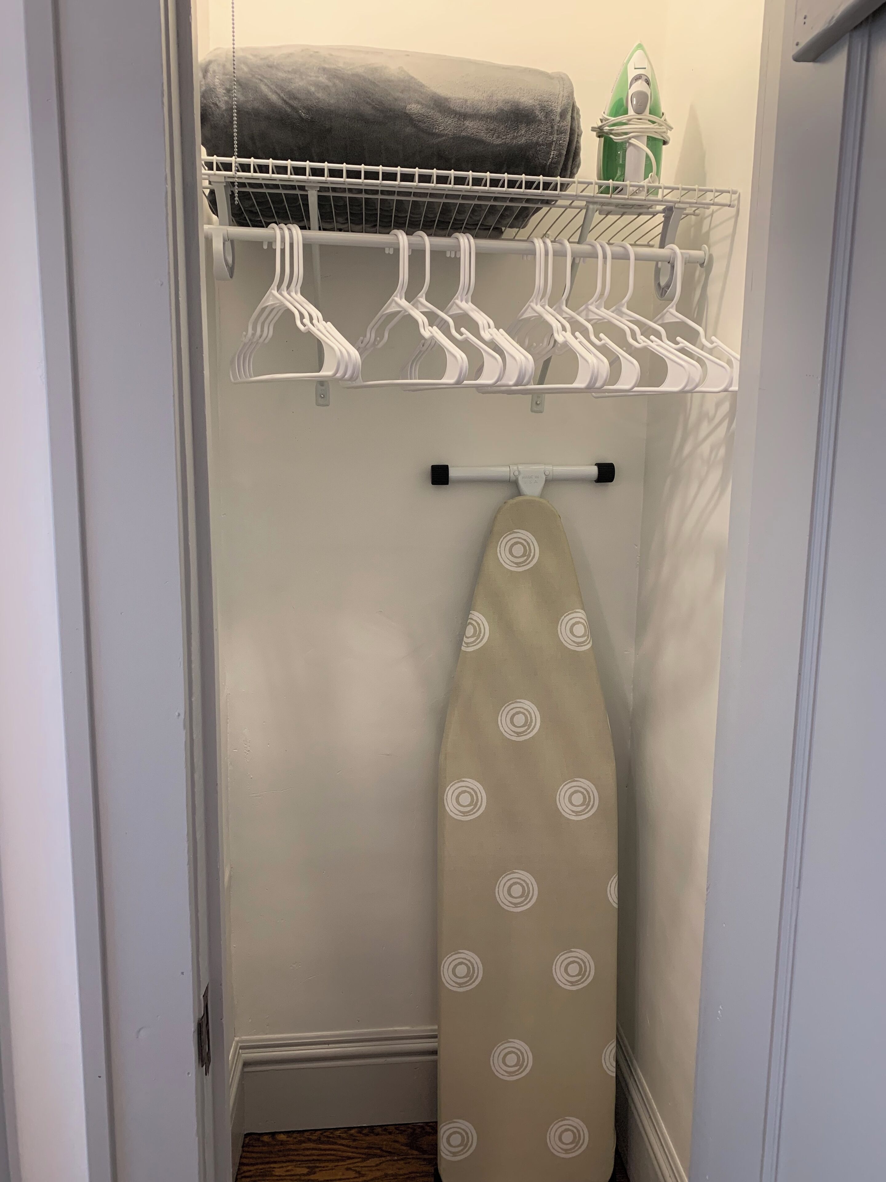 Un petit placard étroit, équipé d’une tringle pour suspendre les vêtements, d’une étagère où est pliée une serviette et d’une planche à repasser.
