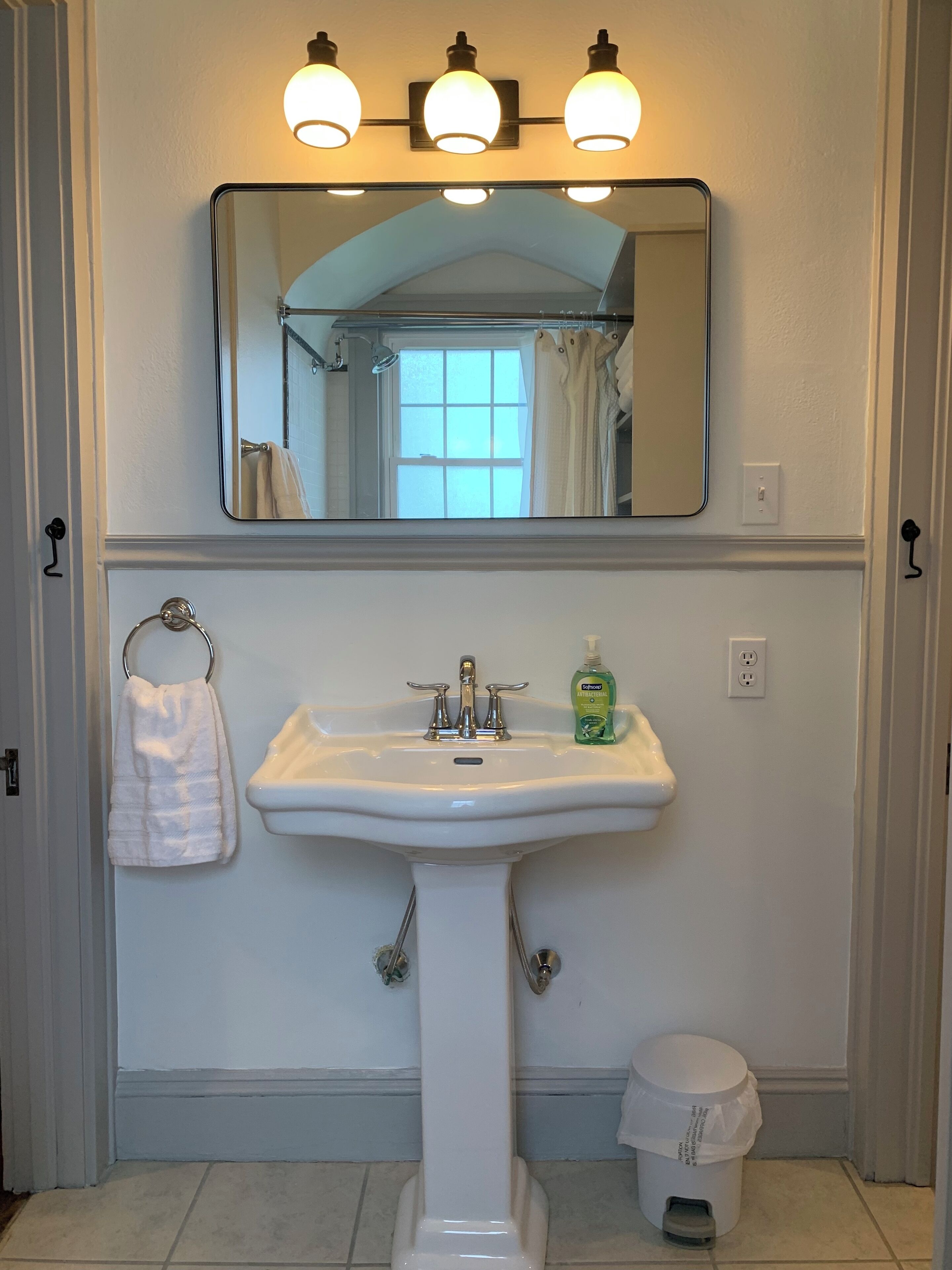 A bathroom with a pedestal sink, a mirror above it, and a window with curtains.