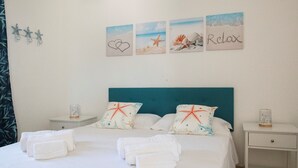 Un lit bien fait, avec du linge de lit et des serviettes blancs, une tête de lit turquoise et des coussins décoratifs ornés de motifs d’étoiles de mer.