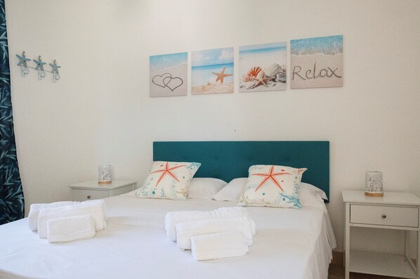 A neatly made bed with white linens and towels, a teal headboard, and decorative pillows with starfish designs. - Trullo Flamingo - Charming fully renovated Villa with private pool (Puglia)