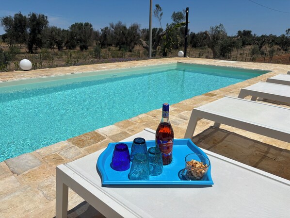 A poolside setting with a tray containing a bottle, glasses, and snacks.