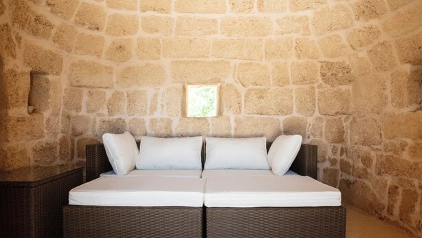 Un lit double dans une chambre aux murs de pierre, avec une petite fenêtre.