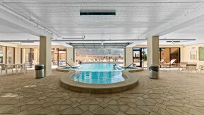 An indoor swimming pool with a tiled floor, surrounded by lounge chairs and a covered seating area.