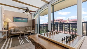 A room with a wooden chess table, a sofa, a painting, and a view of buildings through large windows.