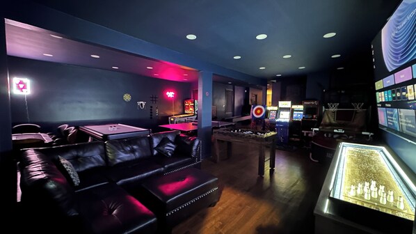 Zona de bar con poca luz, asientos de cuero, juegos de arcade y una vitrina con objetos.