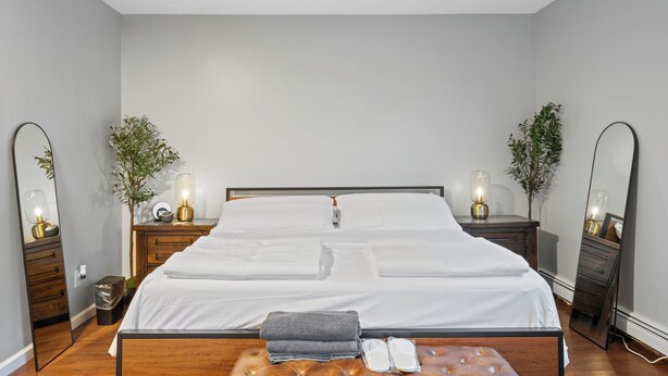 Un lit bien fait, avec du linge de lit blanc, deux tables de chevet avec des lampes et un miroir de chaque côté.