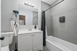 Un baño con inodoro, lavabo, espejo, cortina de ducha y una lámpara sobre el espejo.