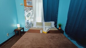 Ein Schlafzimmer mit einem Bett, einem Nachttisch, einer Lampe, einem Vorhang und einem an der Wand montierten Radio.