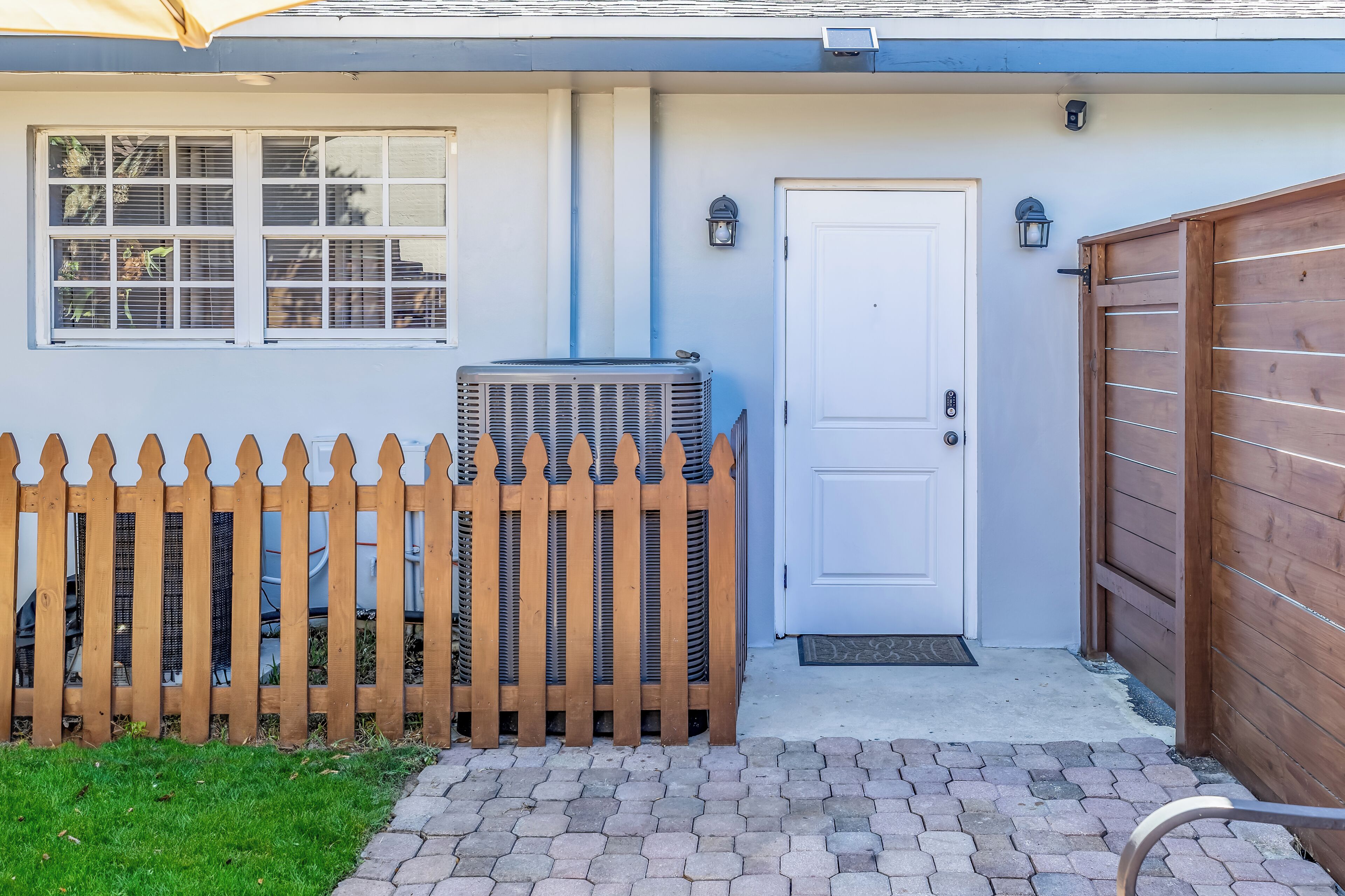 Una casa con puerta blanca, cerca de madera y unidad de aire acondicionado.