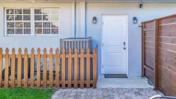 Una casa con puerta blanca, cerca de madera y unidad de aire acondicionado.