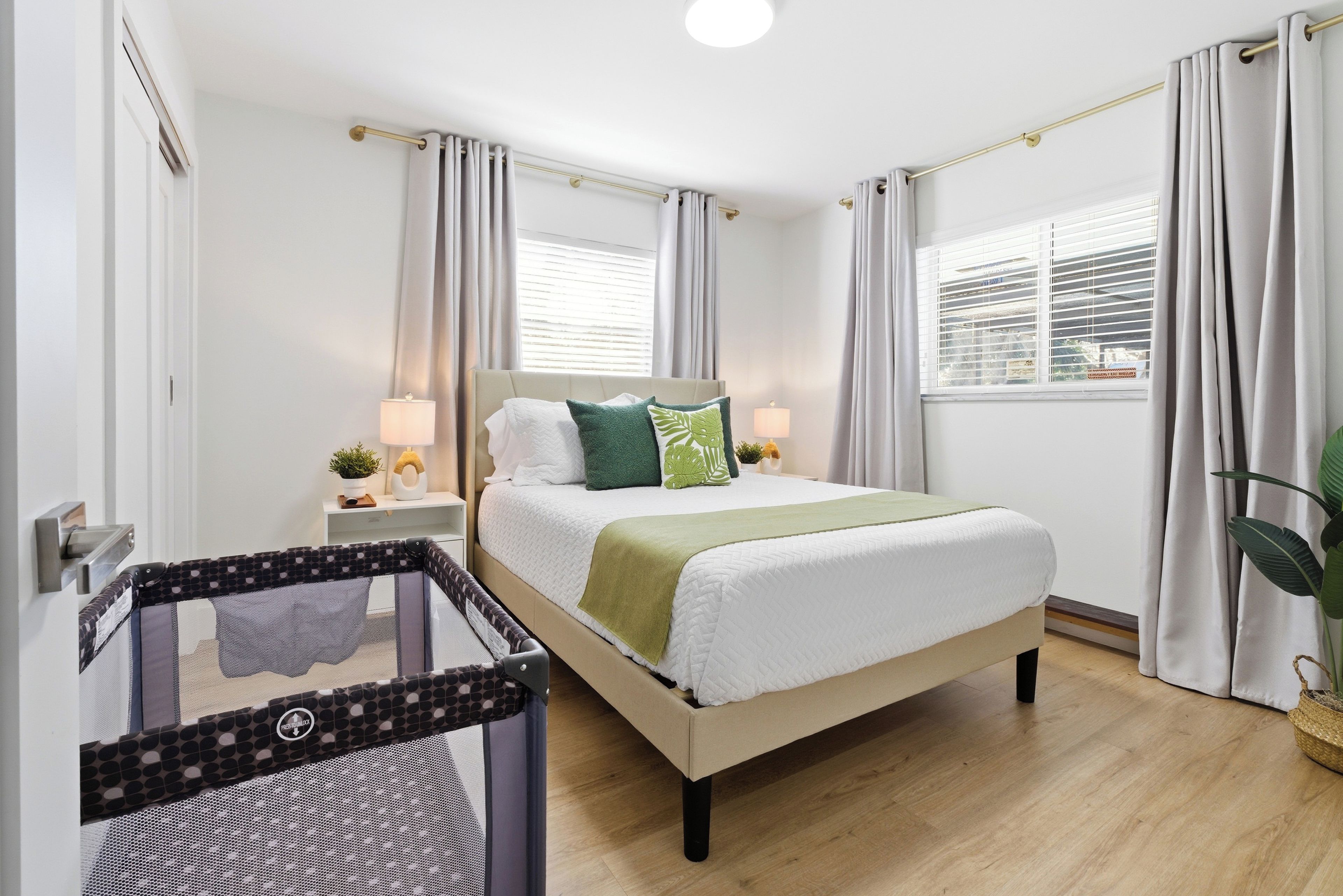 Un dormitorio con cama, cortinas, mesita de noche, lámpara y cuna.
