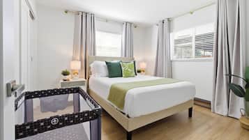 Un dormitorio con cama, cortinas, mesita de noche, lámpara y cuna.