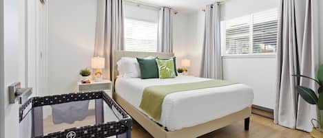 Une chambre à coucher avec un lit, des rideaux, une table de chevet, une lampe et un berceau.