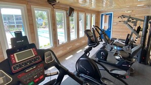 Une salle de sport équipée de machines de cardio, d’appareils de musculation et de grandes fenêtres donnant sur une piscine et un espace extérieur.