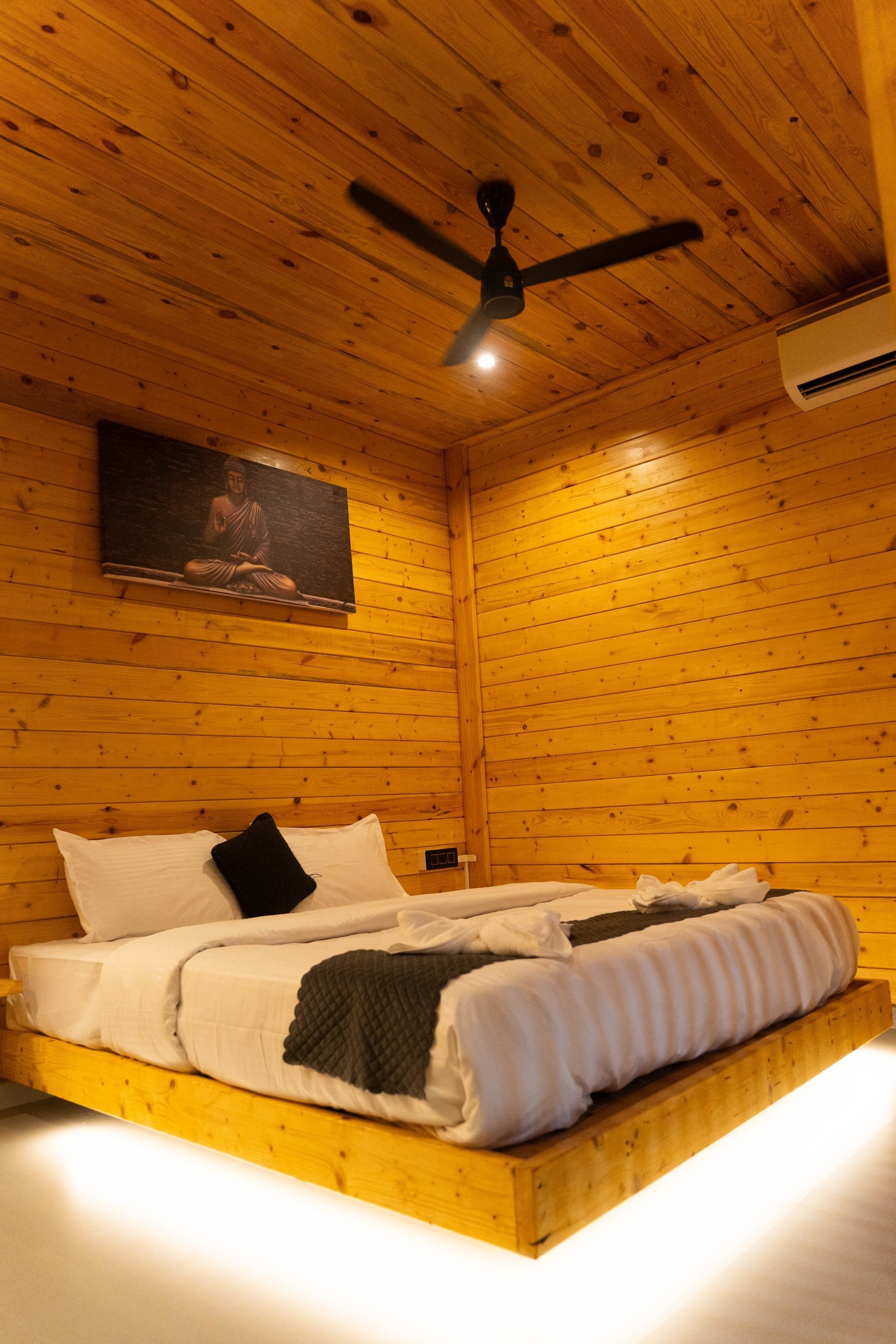 Un dormitorio tipo cabaña de madera con cama, ventilador de techo y aire acondicionado de pared.