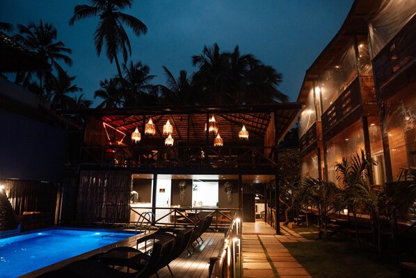 A poolside area with a wooden deck, lounge chairs, and a covered seating area with hanging lights. - Tranquillo By The Beach - Luxury Wooden (Calangute)