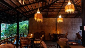 Un restaurante con mobiliario de mimbre, candelabros colgantes y una pared de ladrillo.