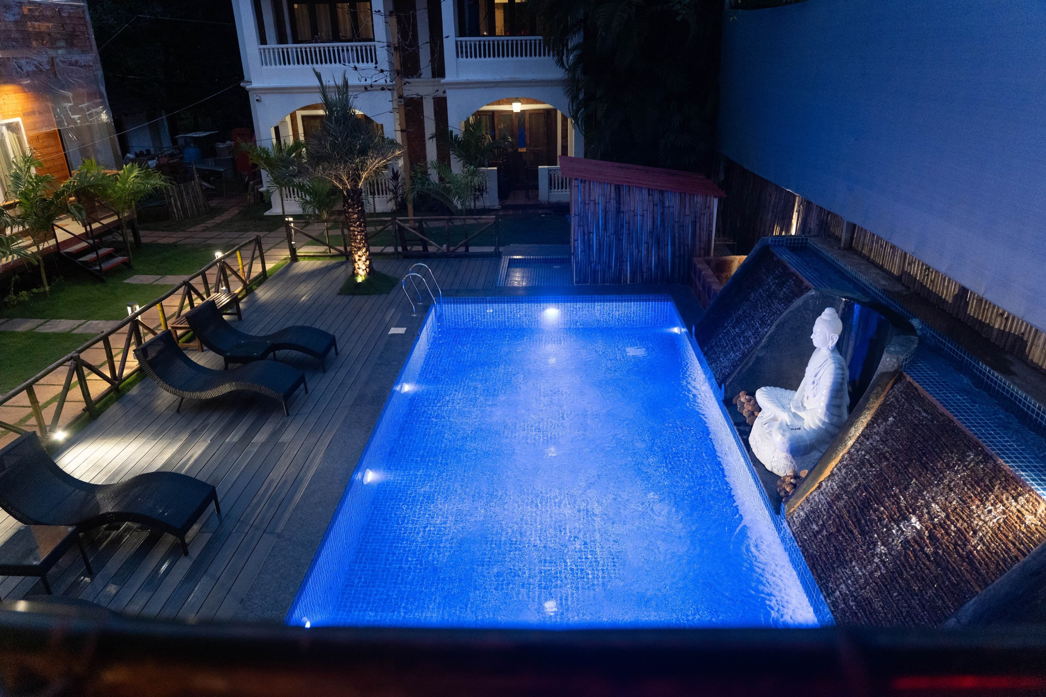 A swimming pool with lounge chairs and a hot tub, surrounded by a deck and a building with a balcony.