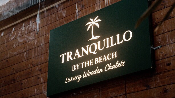 Señal que indica 'TRANQUILLO BY THE BEACH, Cabañas de madera de lujo'.