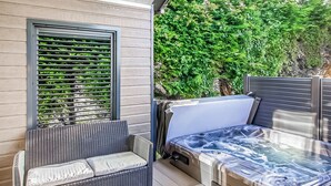 A patio area with a wicker sofa, a hot tub, and a window with blinds. - Pladda Pod with Hot Tub S (Ayr)