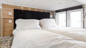 A hotel room with a wooden headboard, two beds, a window, and a ceiling with recessed lighting. - Pladda Pod with Hot Tub S (Ayr)