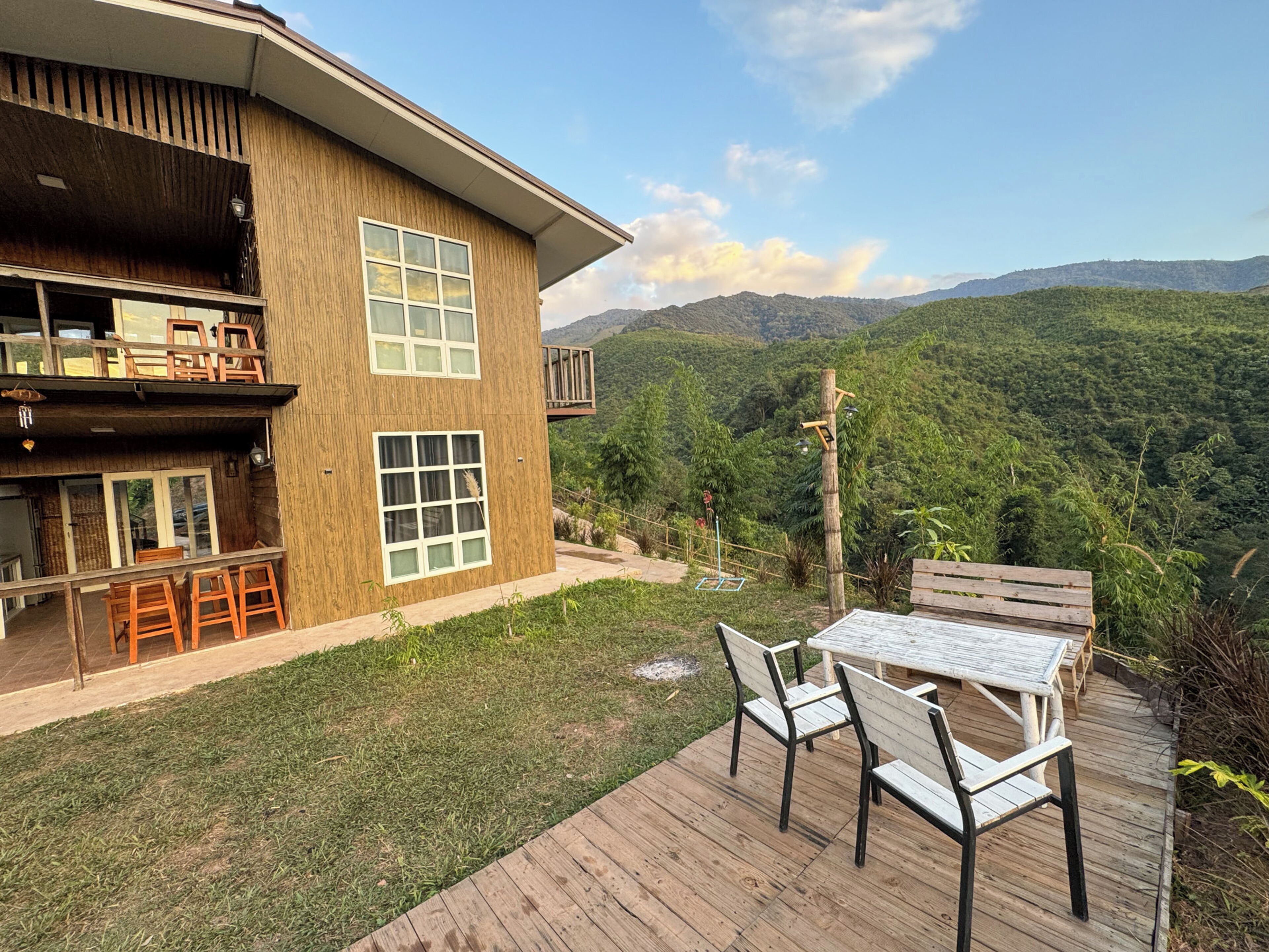 Una casa a due piani in legno con veranda, posti a sedere all'aperto e vista su un paesaggio montano.