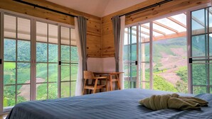 A bedroom with a large bed, wooden beams, and a view of a green landscape through large windows. - Baan Klangkao (Bo Kluea)