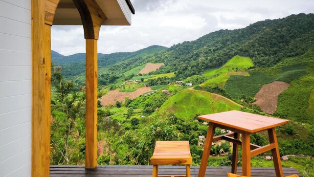A wooden deck with a table and chairs overlooking a lush valley. - Baan Klangkao (Bo Kluea)