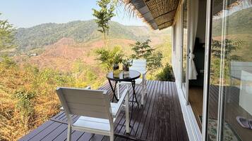 Una terraza de madera con una silla blanca y una mesa, con vistas a un paisaje montañoso.