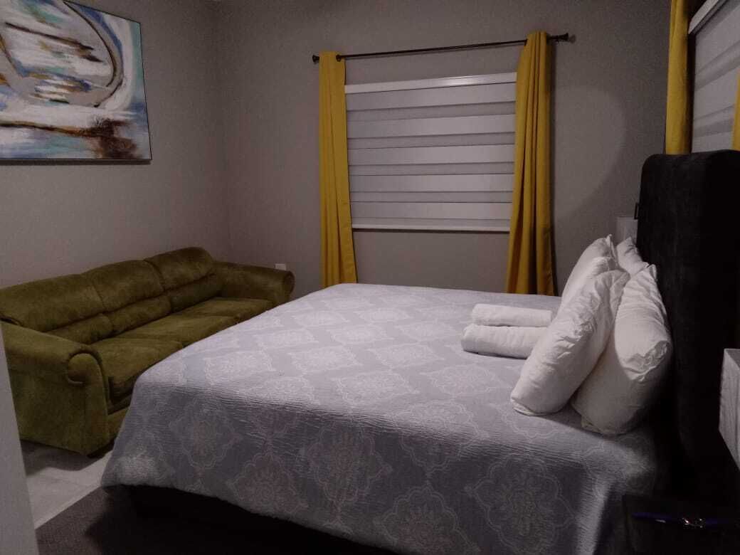 A bedroom with a bed, a green armchair, and a painting on the wall.