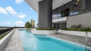 A modern indoor pool with clear blue water, surrounded by a white pool deck and large columns.