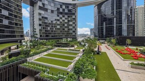 A modern building complex with multiple high-rise structures, a central courtyard with green lawns, and red seating areas.