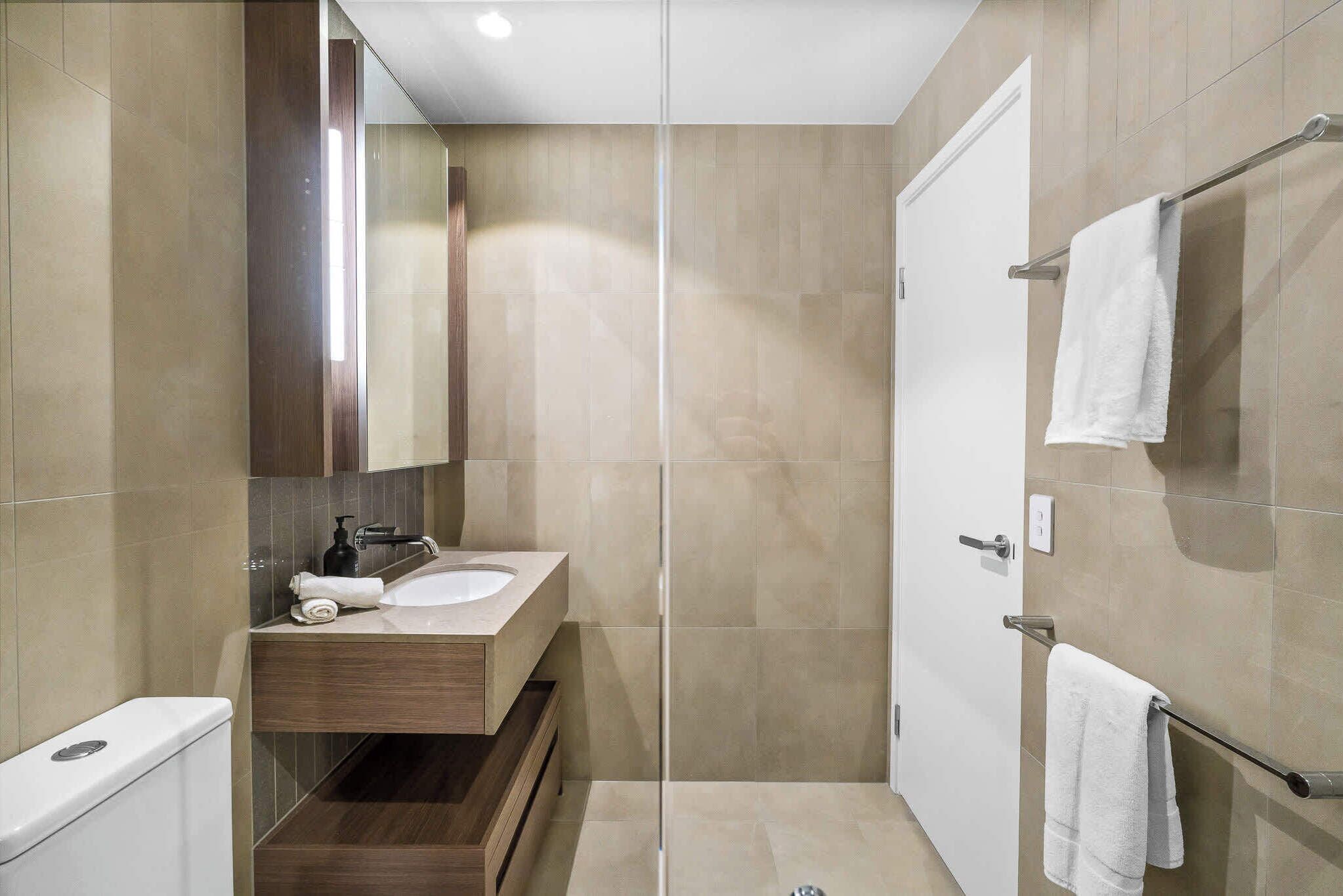 Ein modernes Badezimmer mit Duschkabine aus Glas, Holzwaschtisch und weißer Toilette.