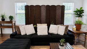 Ein Wohnzimmer mit einer schwarzen Couch, mehreren Kissen, einem Holztisch und zwei runden Gewebepuffen.