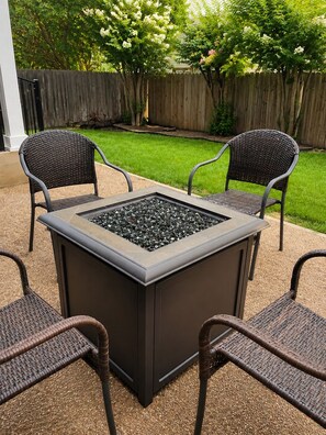 A square outdoor fire pit with a metal frame and a stone top, surrounded by four wicker chairs. - THE ZEN LUXE LOUNGE (Cedar Park)