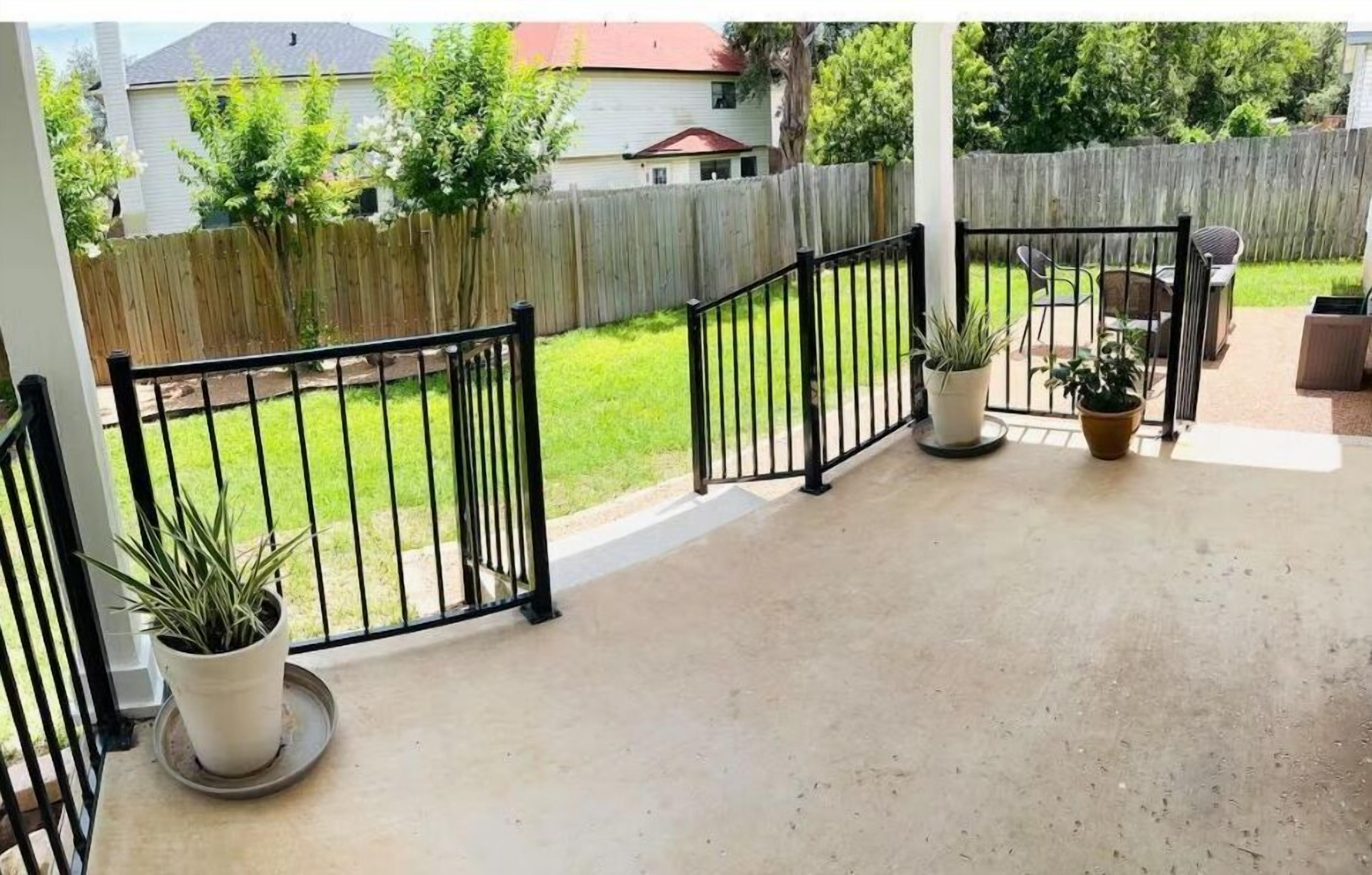 A covered patio area with a concrete floor, potted plants, and a wooden fence in the background.