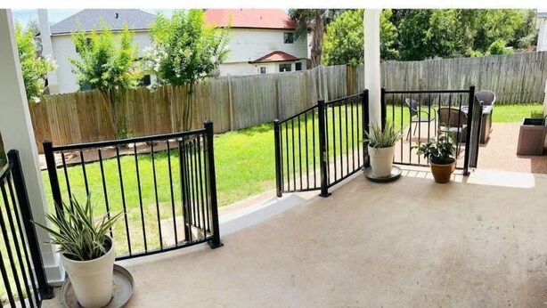 Ein überdachter Patio-Bereich mit Betonboden, Kübelpflanzen und einem Holzzaun im Hintergrund.